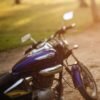 Close-up of a polished motorcycle parked on a sunlit dirt road with green field background.