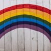 Vibrant rainbow painted on a white wooden wall, symbolizing hope and diversity.